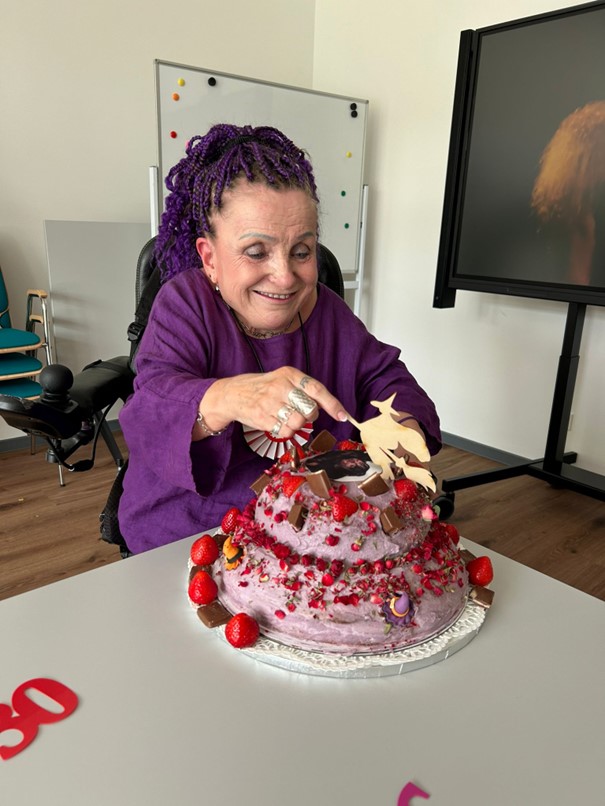 Foto: Barbara schaut sich lächelnd die Torte an, die für sie zum Dienstjubiläum gebacken wurde.
